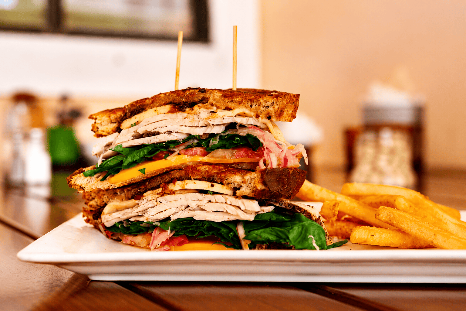 Stacked turkey club sandwich with lettuce, tomato and cheese, served with fries